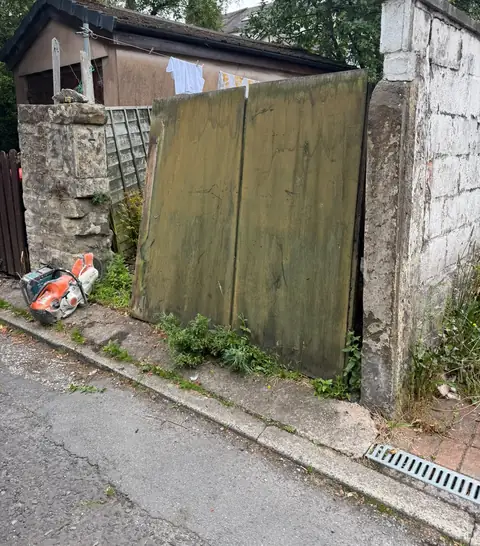 Rotten timber gates between deteriorating stone and rendered piers.